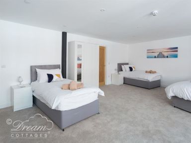 A bedroom with three single beds white bedside tables and a wardrobe at Old Coastguard Apartment 2 in Weymouth