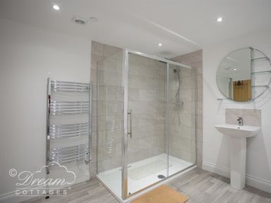 A bathroom with a glass shower enclosure a pedestal sink a round mirror and a chrome towel radiator at Old Coastguard Apartment 2 Weymouth