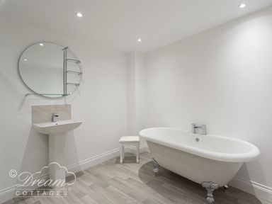 A bathroom with a freestanding bathtub a pedestal sink a round mirror and a small stool at Old Coastguard Apartment 2 in Weymouth