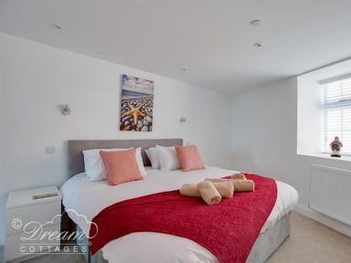A bedroom with a large bed red throw pillows and rolled towels on the bed at Old Coastguard Apartment 2 in Weymouth