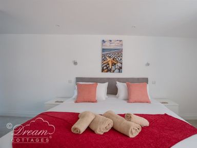 A bedroom with a double bed with red throw and towels and starfish picture on the wall at Old Coastguard Apartment 2 in Weymouth