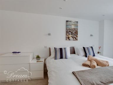 A bedroom with double beds striped pillows rolled towels and framed photo of pebbles on a wall at Old Coastguard Apartment 2 in Weymouth