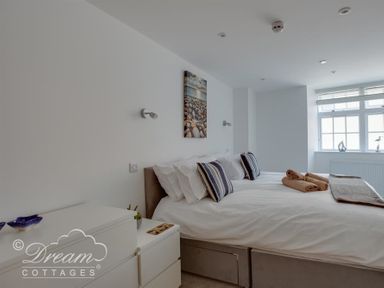 A bedroom with a bed with pillows and towels and a window with decorations at Old Coastguard Apartment 2 in Weymouth