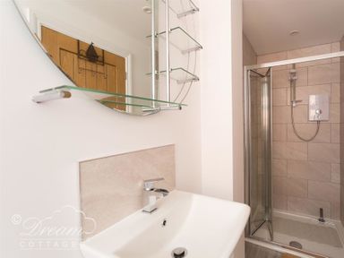 A bathroom with a sink and faucet a mirror with glass shelves and a shower cubicle at Old Coastguard Apartment 2 in Weymouth