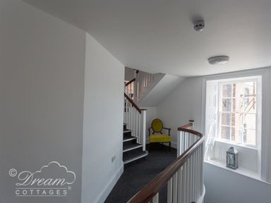 A staircase landing with a yellow chair near a window and white banisters at Old Coastguard Apartment 2 in Weymouth