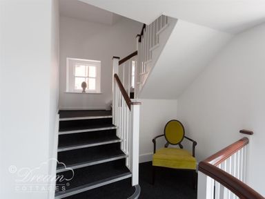 A staircase with dark carpet and white railing and a green upholstered chair at Old Coastguard Apartment 2 in Weymouth