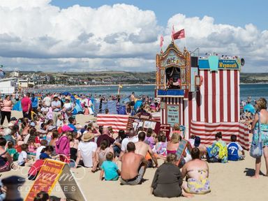 A crowd of people sitting on a sandy beach watching a puppet show at Old Coastguard Apartment 2 in Weymouth