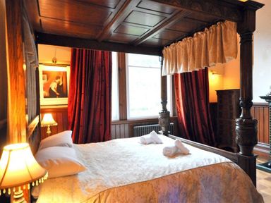 A bedroom with a four-poster bed white rolled towels on the bed red curtains and wooden furniture at The Old Portland Courthouse Portland