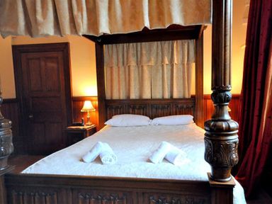 A wooden four poster bed with white bedding and rolled towels in a bedroom with wooden door and lamp at The Old Portland Courthouse in Portland