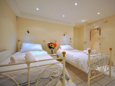A bedroom with two single white metal beds with gold accents a small bedside table with flowers and an open door at The Old Portland Courthouse in Portland
