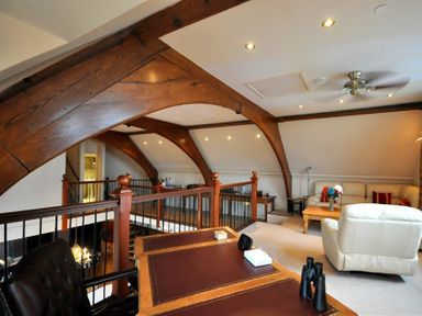 An attic room with wooden beams a desk with chair and binoculars a white armchair and a couch with a coffee table at The Old Portland Courthouse in Portland