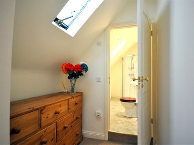 A wooden dresser with flowers in a small hallway with a skylight and an open door leading to a bathroom at The Old Portland Courthouse in Portland