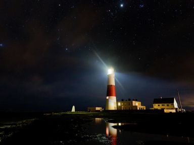 A lighthouse with its light on near buildings under a starry night sky at The Old Portland Courthouse in Portland