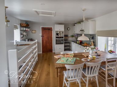A kitchen with a wooden table and chairs a board game on the table and white cabinets at The Old Reading Room in Langton Herring