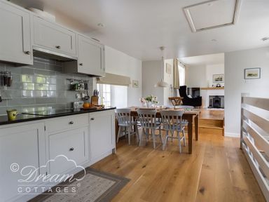 A kitchen with white cabinets and a dining table with chairs and flowers at The Old Reading Room in Langton Herring