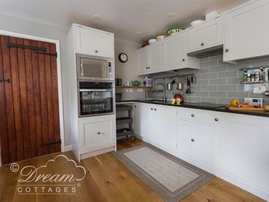 A kitchen with white cabinets a wooden door and appliances at The Old Reading Room in Langton Herring