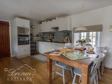 A kitchen with white cabinets a wooden dining table with chairs and a monopoly board game at The Old Reading Room in Langton Herring