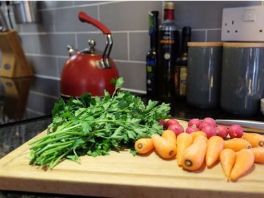 A kitchen countertop with a cutting board holding parsley carrots and radishes and a red kettle in the background at The Old Reading Room in Langton Herring