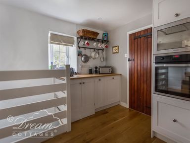 A kitchen corner with white cabinets wooden countertop hanging mugs and pots a wooden door and built in oven at The Old Reading Room in Langton Herring