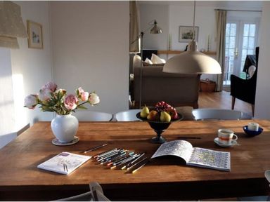 A wooden dining table with colored pencils flowers in a vase a fruit bowl an open coloring book a cup and candle in a living space at The Old Reading Room in Langton Herring