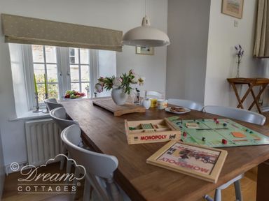 A dining table with a Monopoly board game flowers and cups near a window at The Old Reading Room in Langton Herring