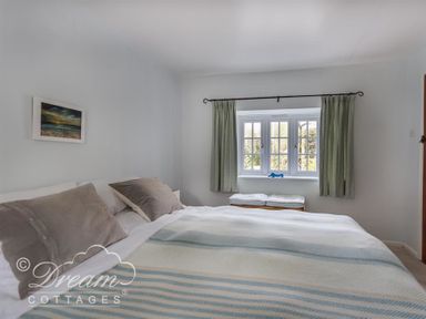 A bedroom with a bed with pillows a window with green curtains and a bench at The Old Reading Room in Langton Herring