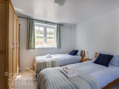 A bedroom with two single beds side by side and a wooden wardrobe by a window at The Old Reading Room in Langton Herring