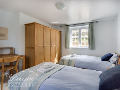A bedroom with two single beds a wooden wardrobe a desk and chair and a window with curtains at The Old Reading Room in Langton Herring