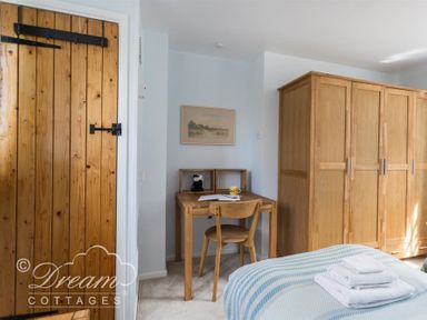 A bedroom with a wooden door wooden desk and chair wooden wardrobe and a bed with folded towels at The Old Reading Room in Langton Herring