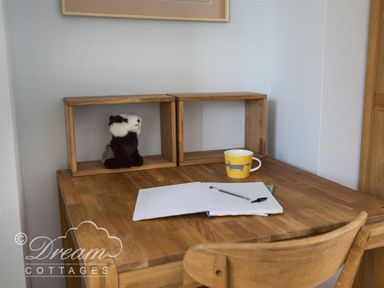 A wooden desk with two wooden shelves a stuffed animal an open notebook a pencil and a yellow mug at The Old Reading Room in Langton Herring