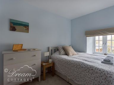 A bedroom with a single bed near a window a small wooden side table with a lamp and mug a light colored dresser with items on top and a painting on the wall at The Old Reading Room in Langton Herring