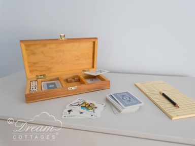 A wooden box with playing cards and dice on a table with a score pad and pencil at The Old Reading Room in Langton Herring