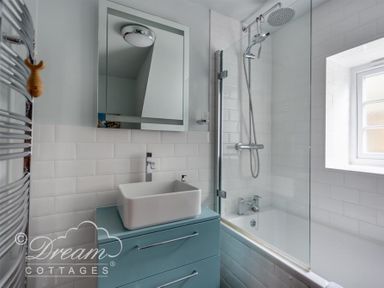 A bathroom with a bathtub shower combination and a sink on a blue vanity at The Old Reading Room in Langton Herring
