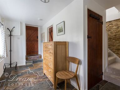 An entryway with a wooden chest of drawers chair coat rack and wooden doors with stone flooring and stairs at The Old Reading Room in Langton Herring