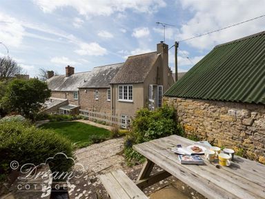 An outdoor area with a picnic table, cups, plates, a book, a stone wall, paths, and a garden at The Old Reading Room in Langton Herring