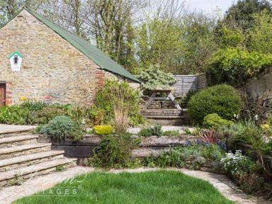 A garden with stone steps, green plants, and a picnic table near a stone building at The Old Reading Room in Langton Herring