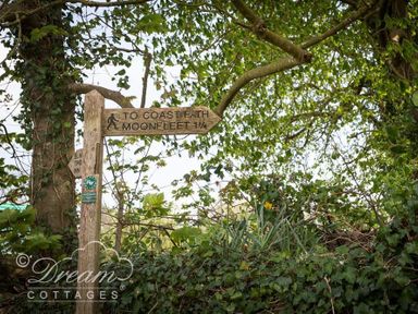 A wooden signpost pointing to coast path and moonfleet among trees and greenery at The Old Reading Room in Langton Herring