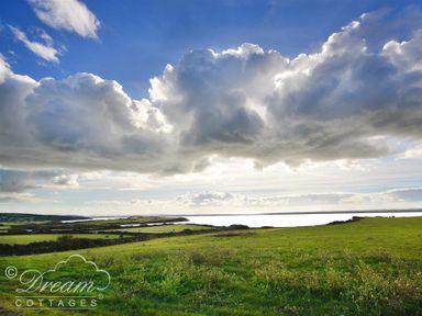 A grassy field with a body of water and large clouds in the sky at The Old Reading Room in Langton Herring