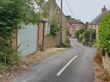 A narrow paved road with houses and greenery on both sides at The Old Reading Room in Langton Herring