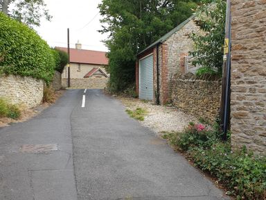 A narrow paved road with stone walls plants and a garage door at The Old Reading Room in Langton Herring