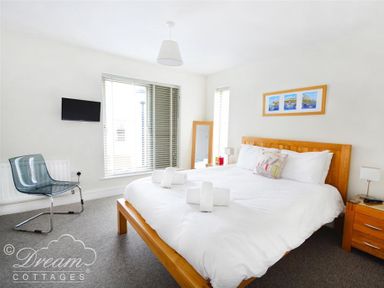 A bedroom with a wooden bed frame and white bedding a chair a wall mounted tv and a framed picture above bed at Olympic Cottage in Portland