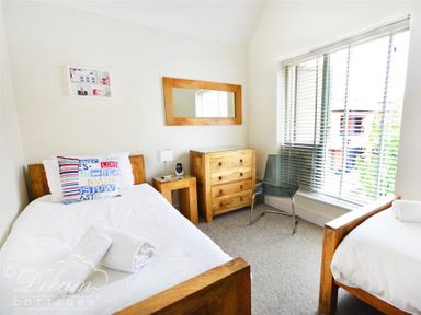 A bedroom with two single beds a wooden chest of drawers a chair and a window with blinds at Olympic Cottage Portland