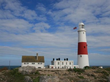 A white lighthouse with a red stripe and two adjacent white buildings on a rocky coastline at Olympic Cottage in Portland