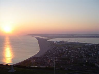 A coastline with a long sandy beach and a town by the shore at sunset at Olympic Cottage in Portland