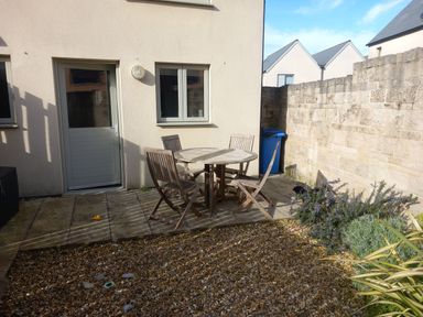 A small patio with round wooden table and four chairs outside a house with beige walls and a stone wall in the background at Olympic Cottage in Portland