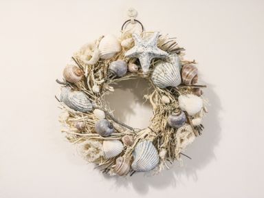 A decorative wreath made of shells starfish and twigs hanging on a white wall at Osprey House Portland in Portland