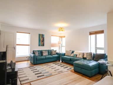 A living room with teal sofas a patterned rug a floor lamp and windows with blinds at Osprey House Portland