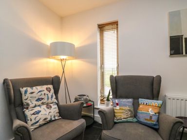 A corner of a room with two gray armchairs each with decorative cushions a floor lamp a small round table with a radio and a plant by a window with wooden blinds at Osprey House Portland in Portland