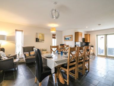 A dining room with a wooden table set with plates and glasses surrounded by chairs next to a sitting area with armchairs and a kitchen area with wooden cabinets at Osprey House Portland in Portland