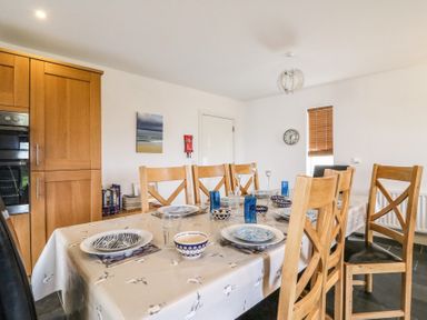 A dining room with a table set for six people wooden chairs and kitchen cabinets in the background at Osprey House Portland